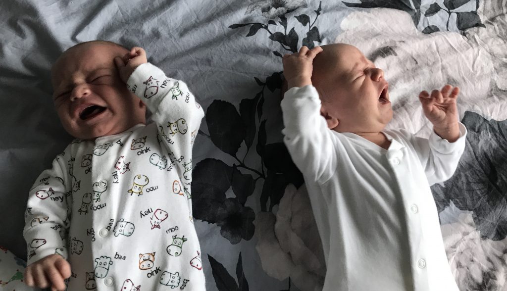 Newborn twins lying on a bed crying facing away from each other