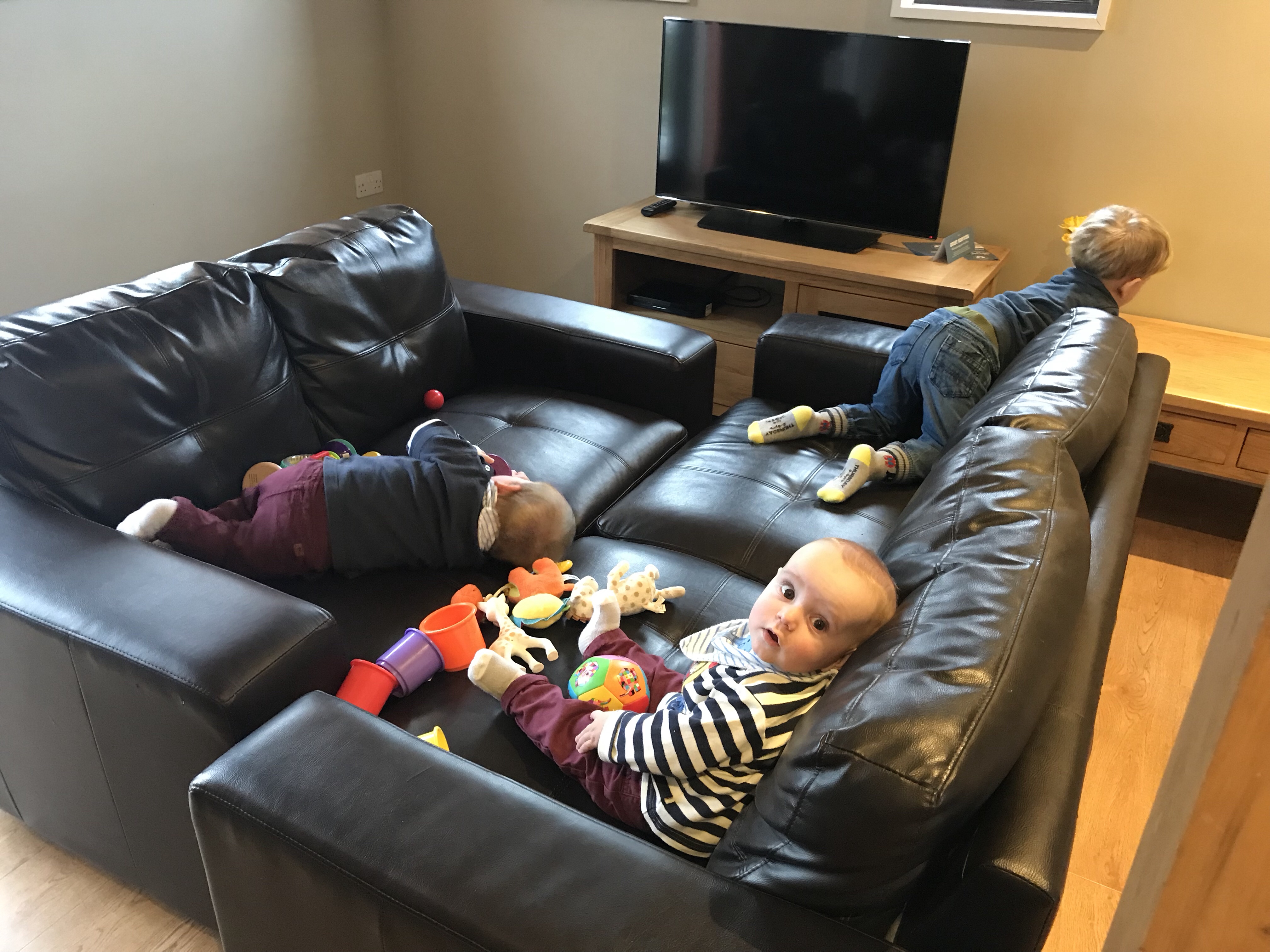 Toddler and baby twins on a makeshift sofa playpen in a St David's  lodge