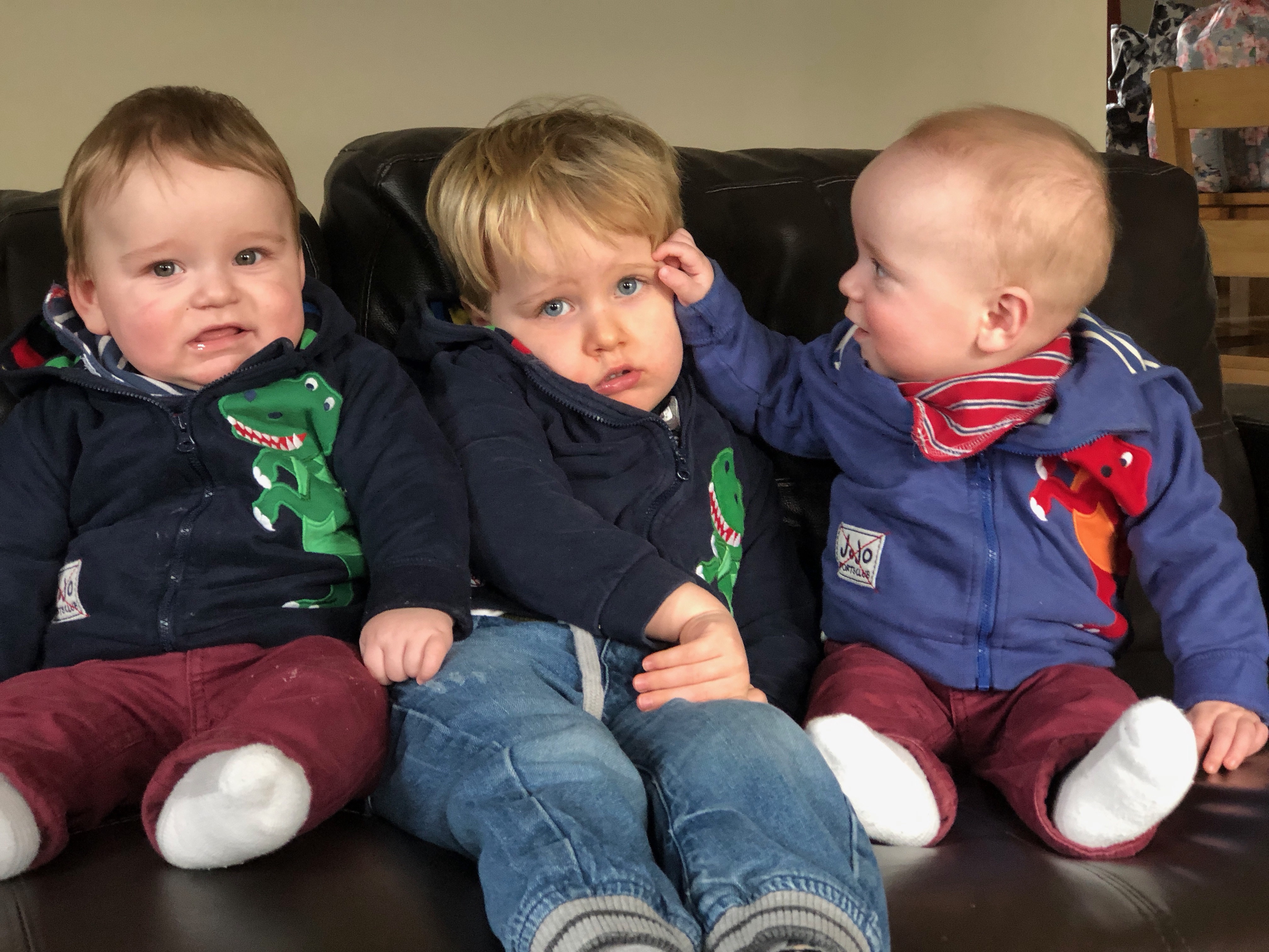 A toddler not looking happy having his photo taken with his twin brothers
