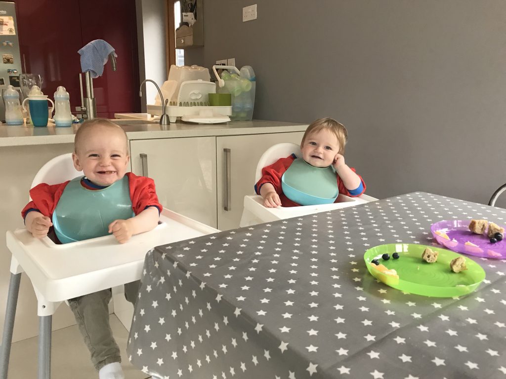 Grey Messy Me oil cloth table cloth on a table with twin babies in a mess with food at their high chairs