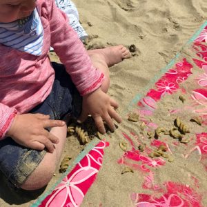 Toddler dropping pasta in the sand on a beach