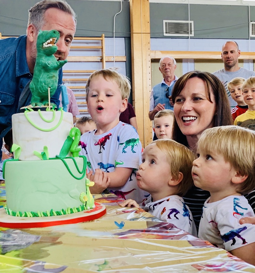 Four year old and two year old twins blow out the candles on their dinosaur cake at a kids' birthday party