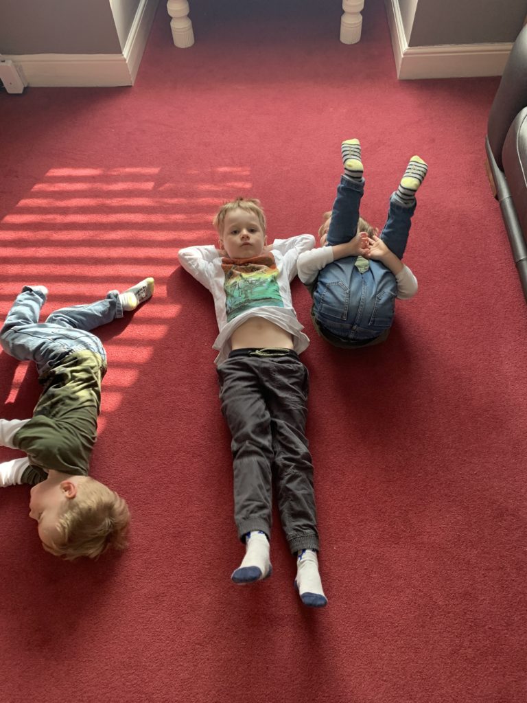 Twin toddlers and their four year old brother lie on the lounge floor