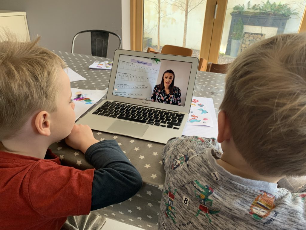 Four year old and two year old brothers watch a phonics You Tube video on a laptop