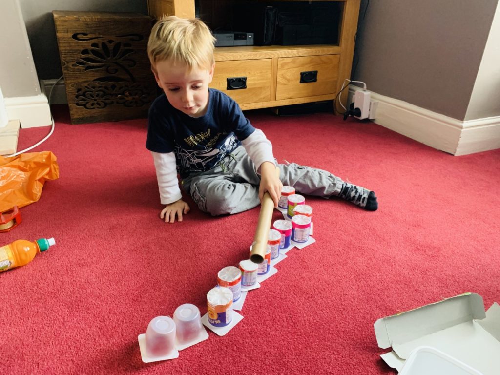 Toddler doing some junk modelling with yoghurt pots in a bid to keep toddlers entertained at home