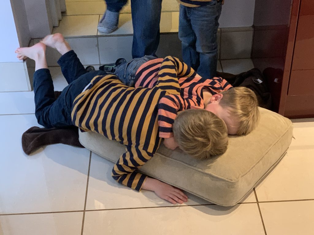 Twin toddlers bring sofa cushion into the kitchen to lie on the floor