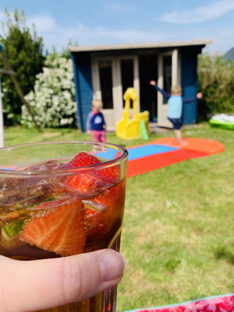 Glass of pimms in the garden with children playing on a slip n slide