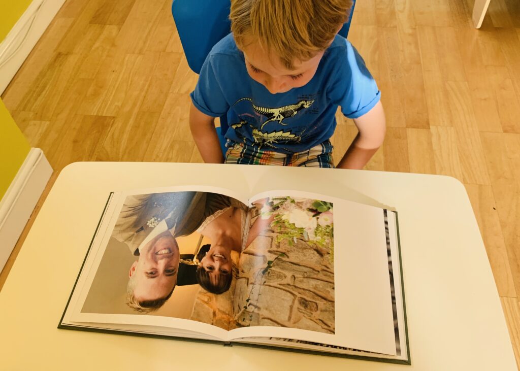 Little boy looking at a wedding picture of his mum and dad in a photo book