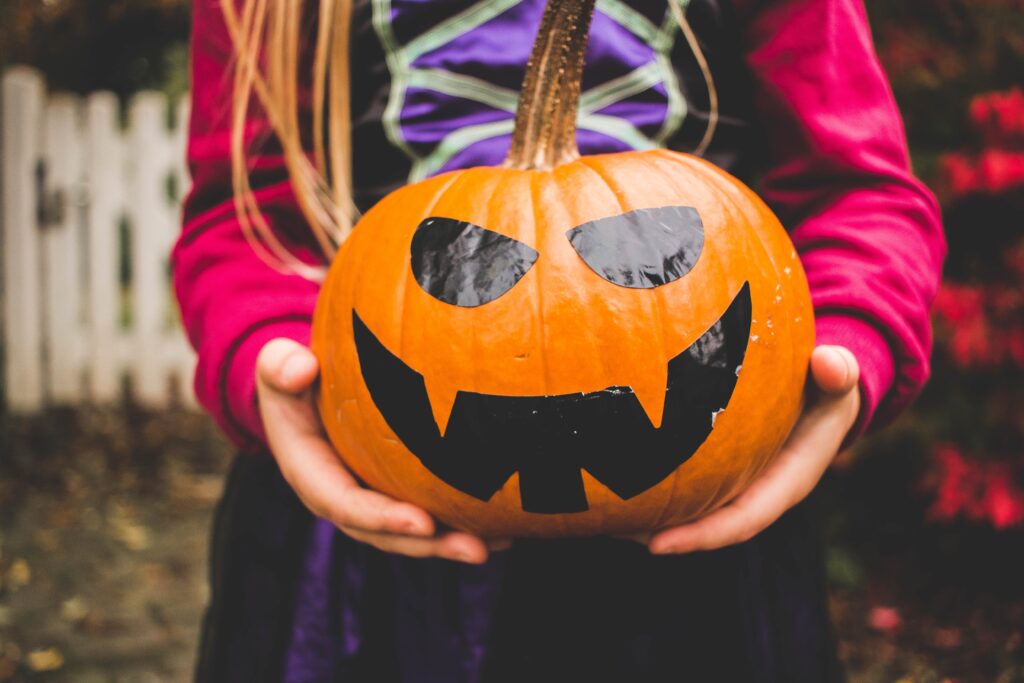 A pair of child's hands holding a pumpkin with a black face on it