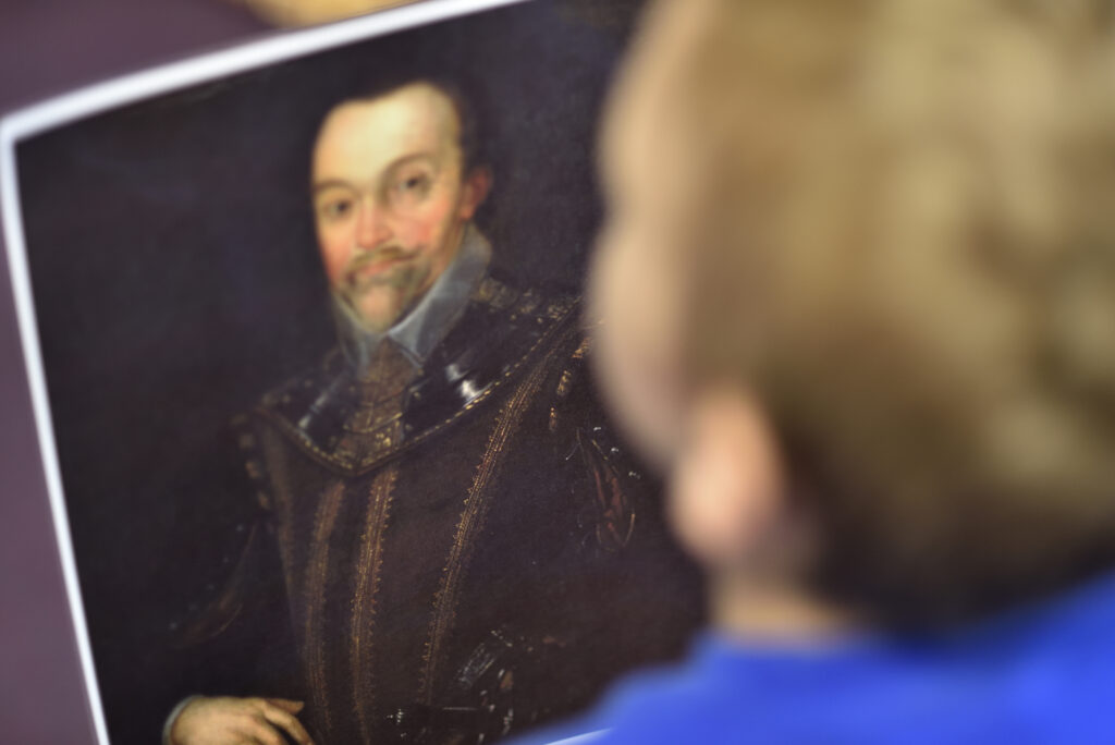 The back of a head of a child looking at an old painting of a man as a part of an educational programme at The Box in Plymouth