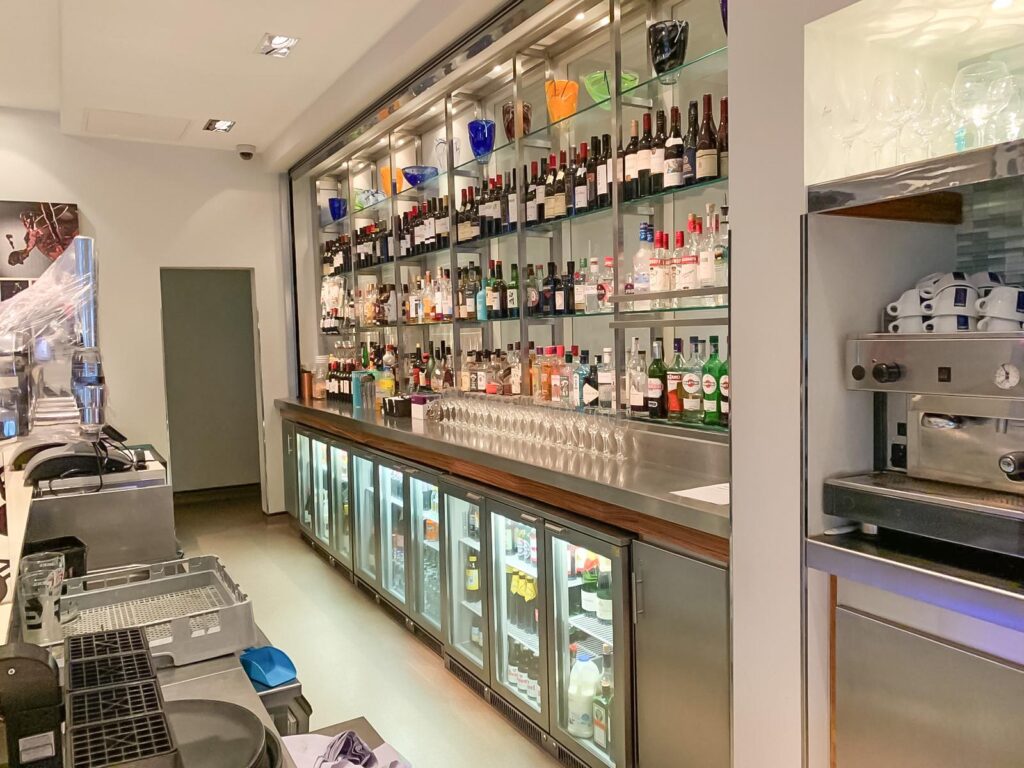 Behind a bar at the Holiday Inn with shelves of drinks and fridges