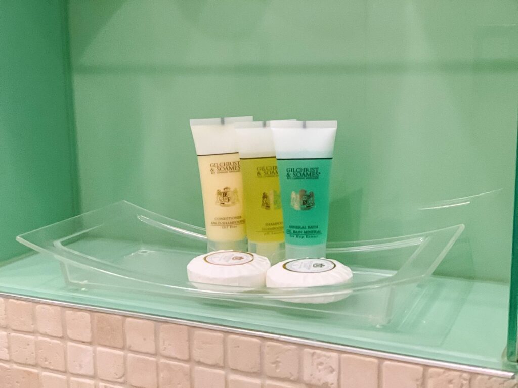 Glass shelf in a bathroom with three different coloured bottles of toiletries