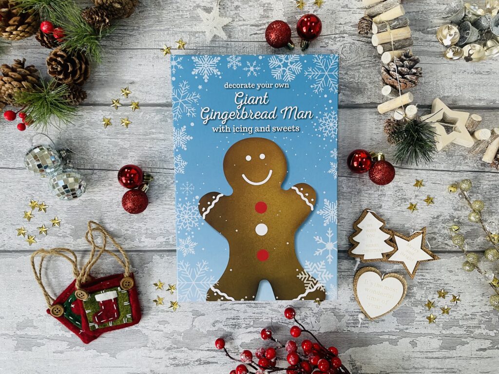 Giant gingerbread man decorating set in a blue box surrounded by Christmas decorations