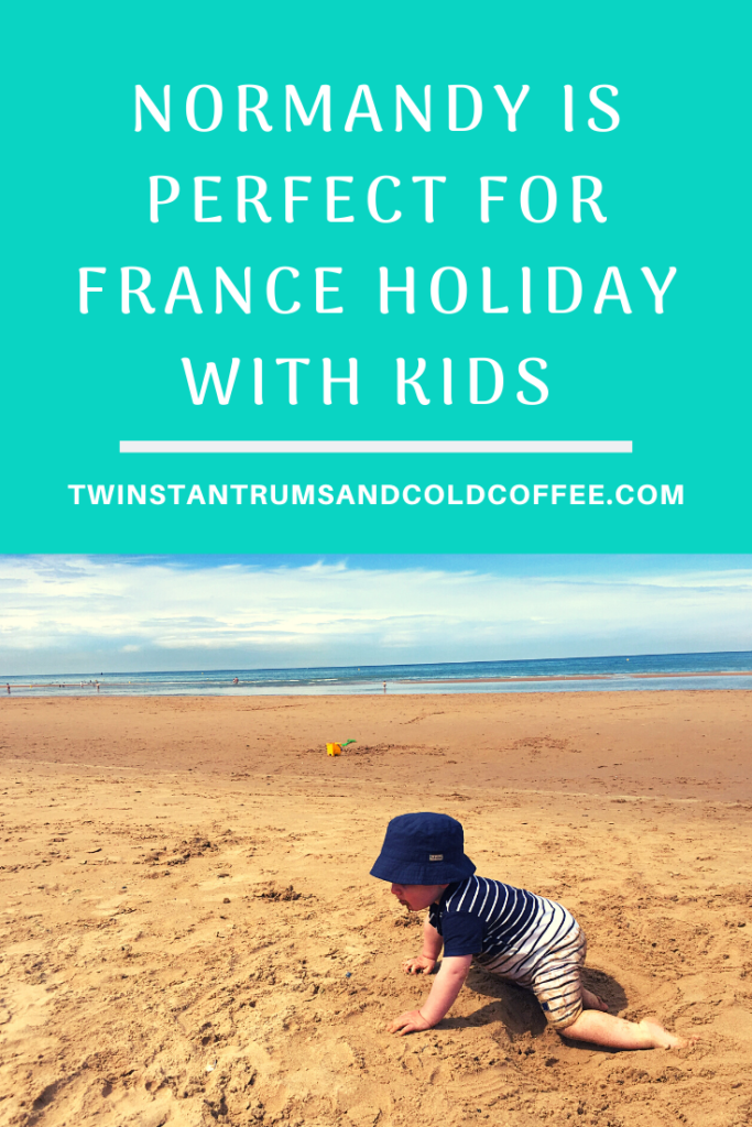 PIN image of a little toddler crawling along the sand with the sea in the background in Normandy