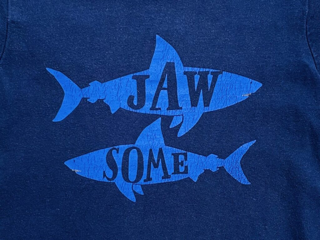 The word 'jawsome' in two sharks as a slogan on a navy shirt