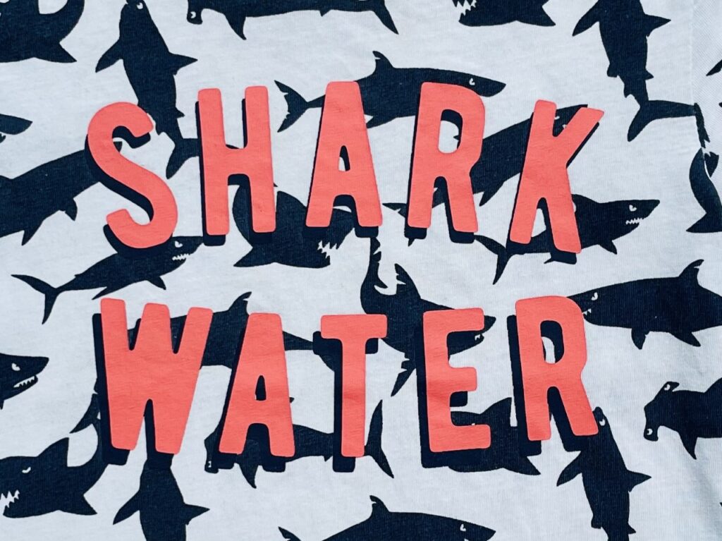 Pink 'shark water' slogan on a white t-shirt with navy sharks on it