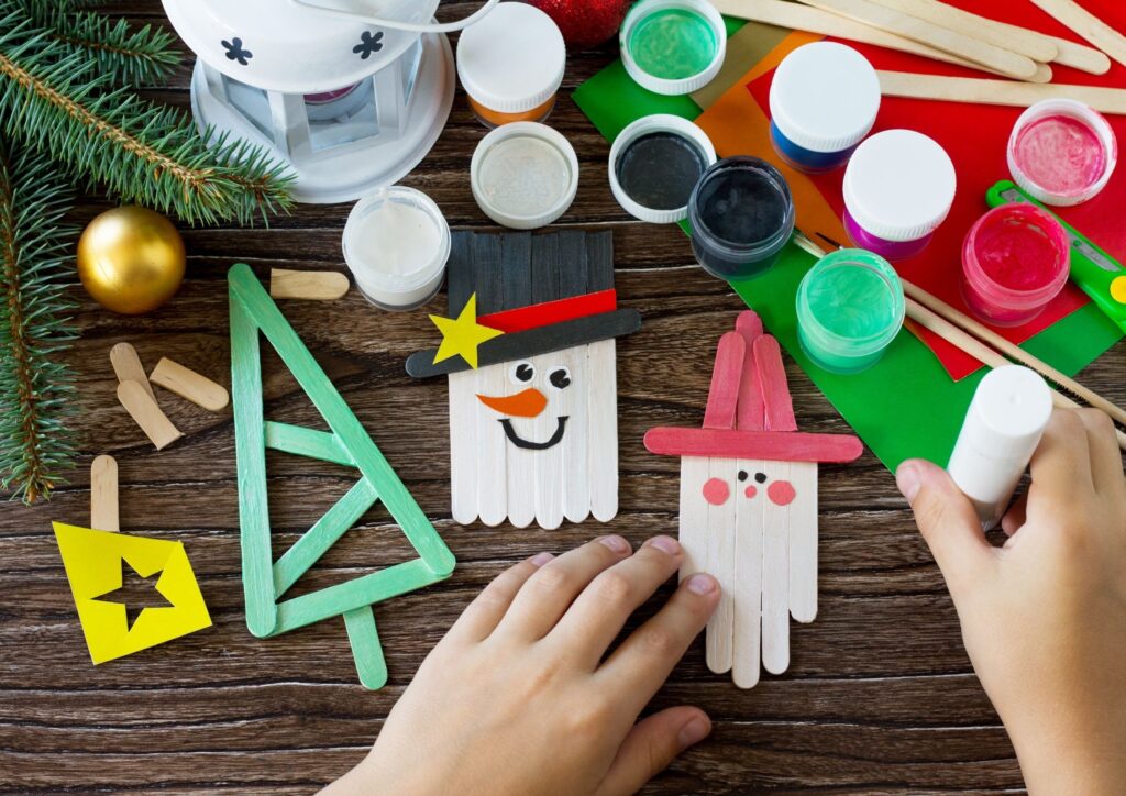 Table of Christmas crafts, paints and snowmen, santa and tree made out of lolly sticks. An idea for Christmas Eve Boxes.