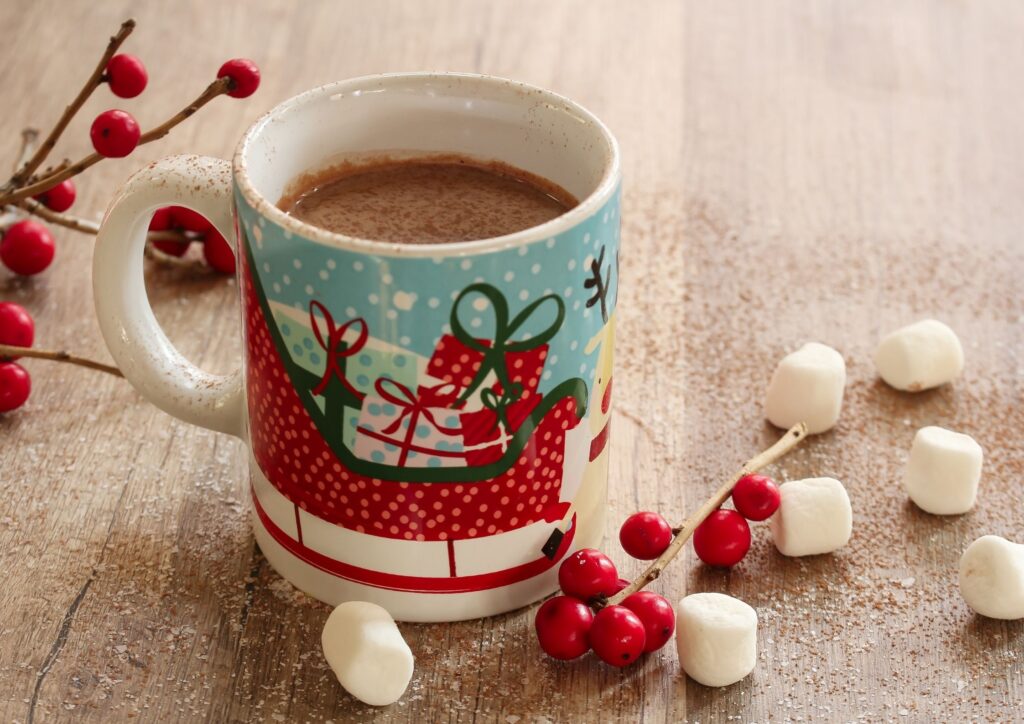 Christmas mug with hot chocolate and marshmallows next to it. An idea for Christmas Eve Boxes.