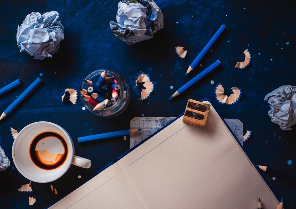 A note pad surrounded by colouring pencils on a dark blue background. An idea for Christmas Eve Boxes.