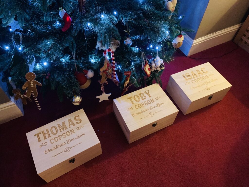 Personalised wooden Christmas Eve boxes lined up under a Christmas tree