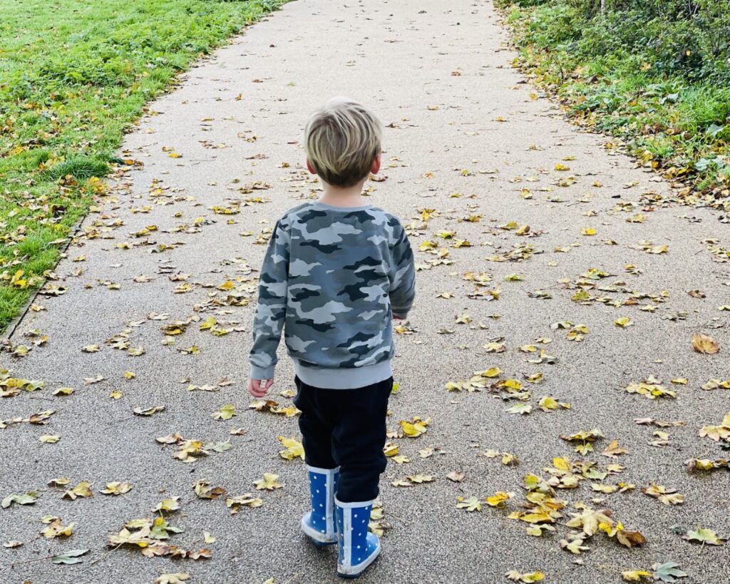 Little boy in wellies walking along a leaf-covered path as a Plymouth place to visit in Tier 3