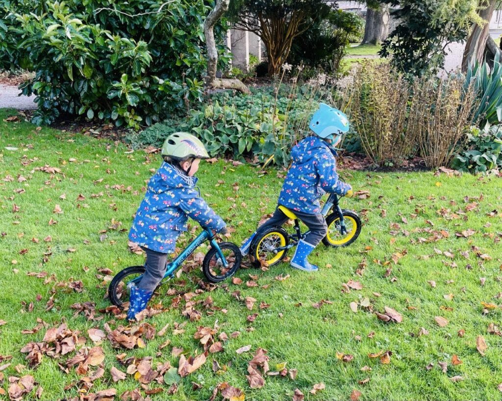 Twin boys riding balance bikes on the grass