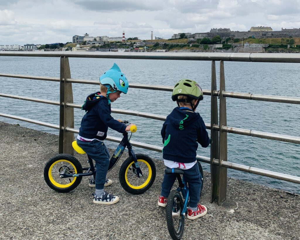 Two little boys on balance bike near a fence on a pier into Plymouth Sound