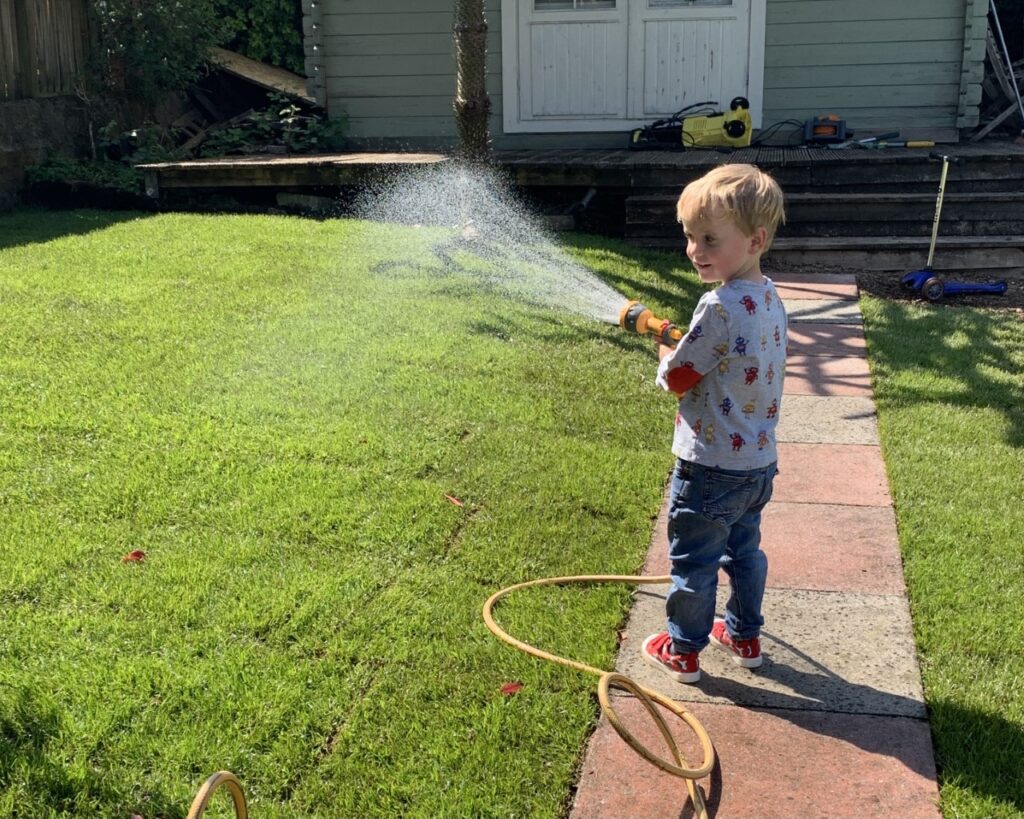 Toddler is encouraged to be playing outside by watering the grass