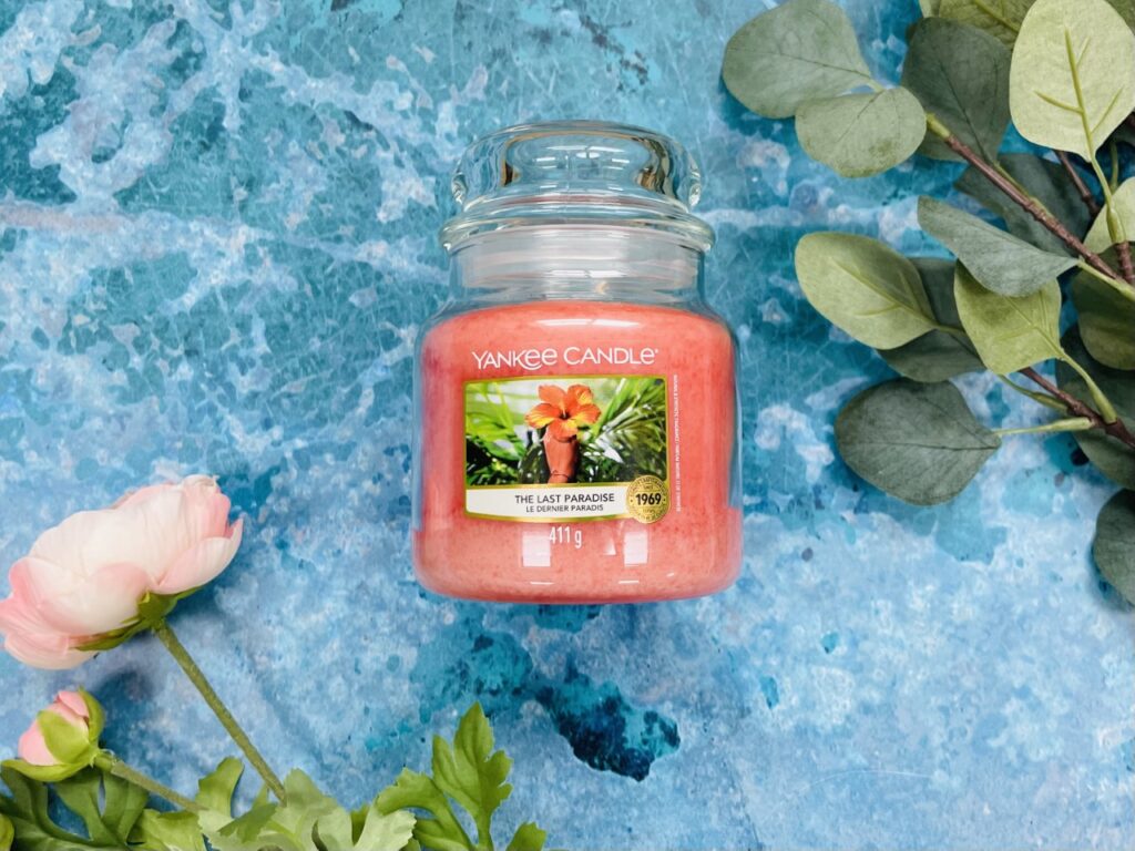 Pink yankee candle in a glass jar on a blue background with flowers and leaves