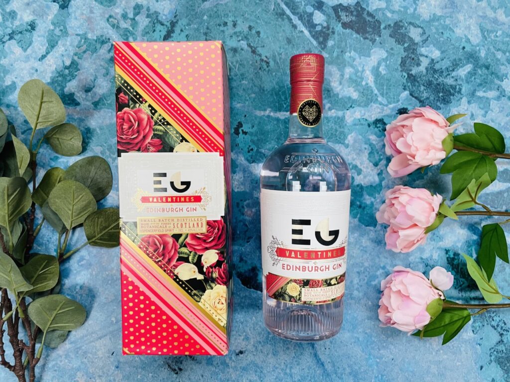 Bottle of Edinburgh gin with the box on a blue background and flowers for Valentine's Day in lockdown