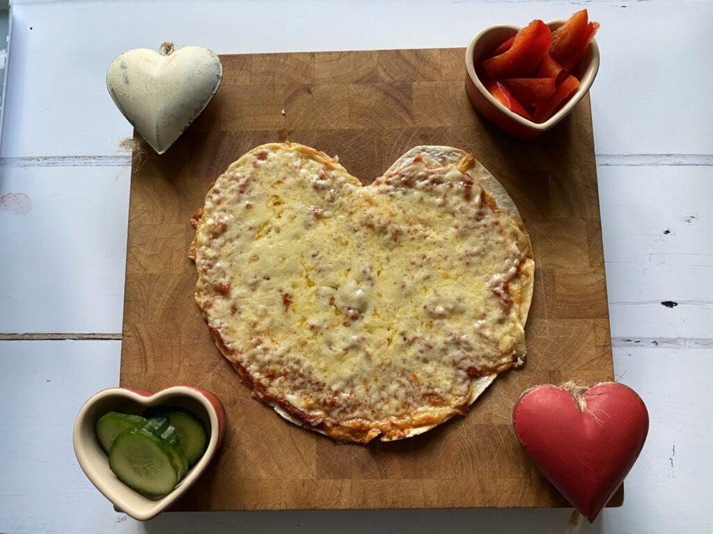 Heart shaped pizza on a wooden board as an idea of how to celebrate Valentine's Day in lockdown