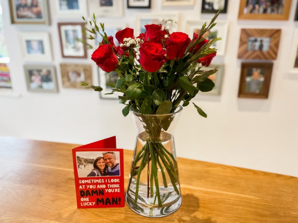 Roses and a card with photo frames in the background as an idea of how to celebrate Valentine's Day in lockdown