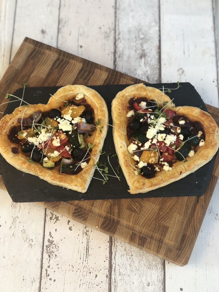 Heart shaped veggie tarts on a black slate plate and wooden board