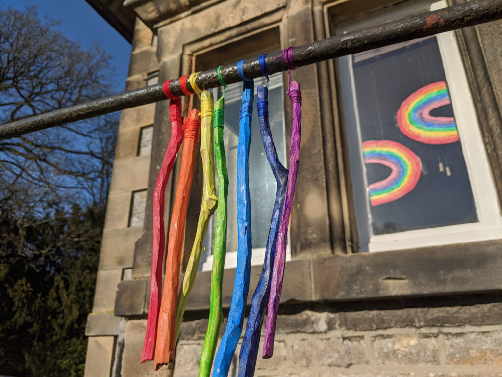 Sticks painted in rainbow colours hanging on a pole, as an activity to do in a half term in lockdown