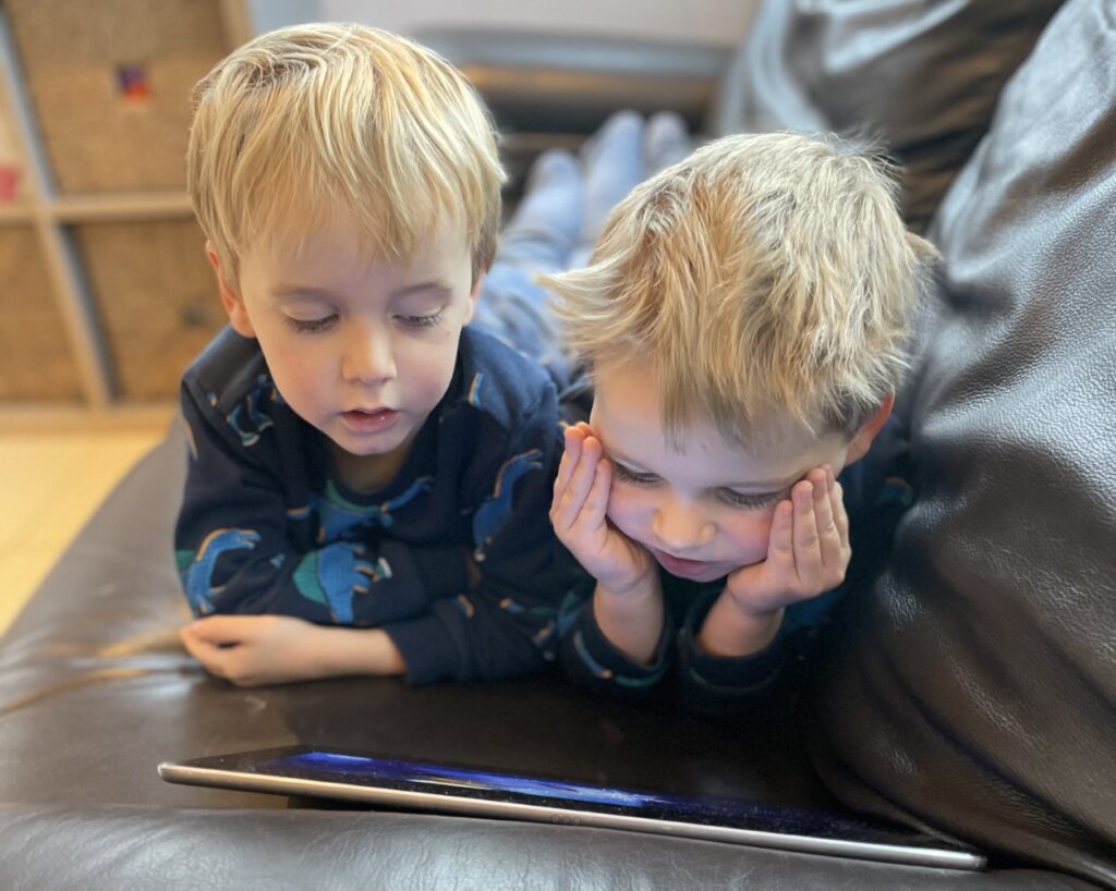 Three year old twin boys lying on a settee and watching the ipad