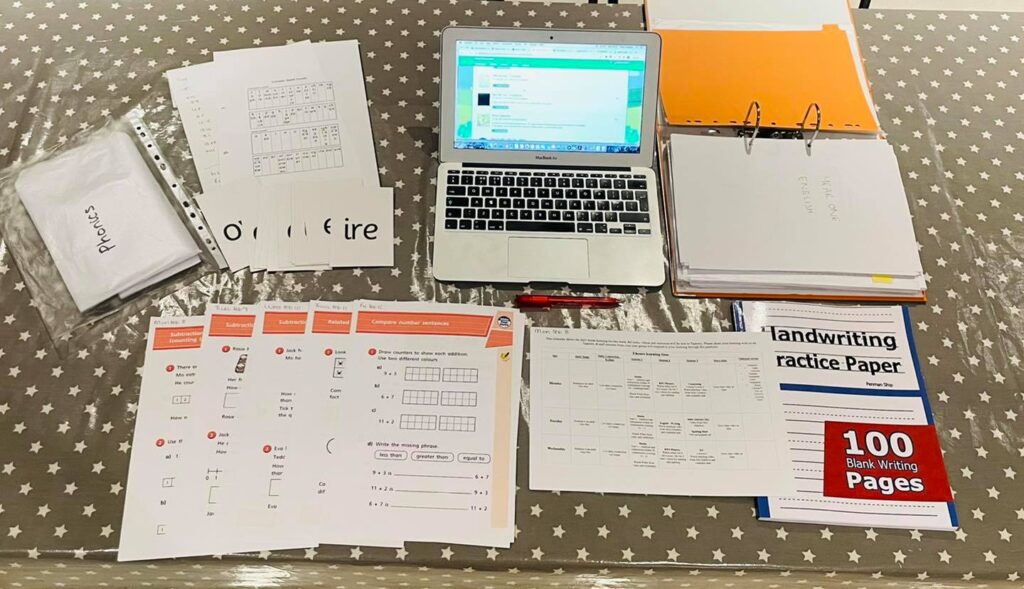 preparation for a week of homeschooling including a laptop, worksheets and print outs on a kitchen table