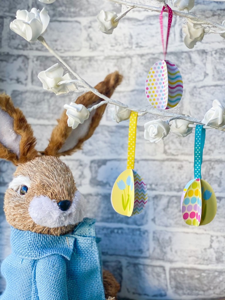 A cuddly rabbit toy next to some hanging easter egg decoration craft