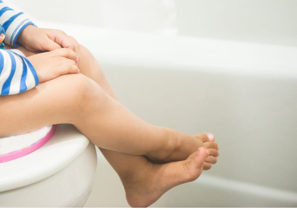 Toddler legs hanging off the edge of a toilet with a toddler seat