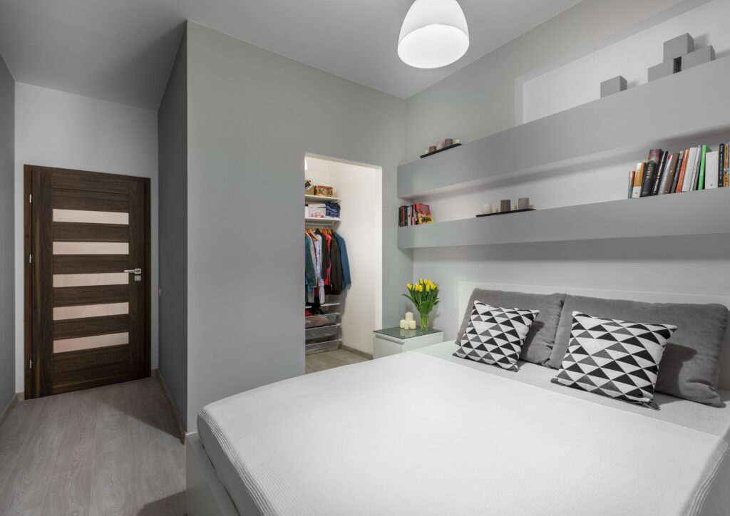 White bed against grey walls and shelves in a bedroom