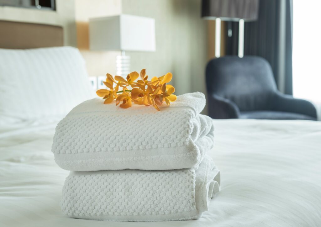 A set of folded white towels with flowers on the top on a bed in a spare room for guests