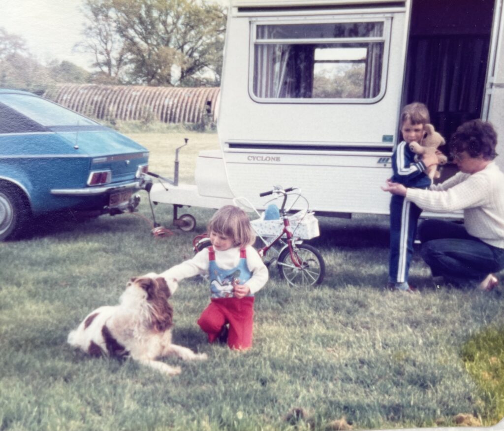 Old pic of a little girl about 2 playing with a dog outside a caravan