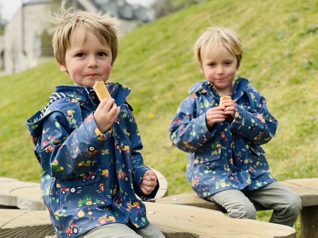 Potty training twins doesn't mean they're both ready at the same time.Twin boys on a park bench eating a biscuit. 