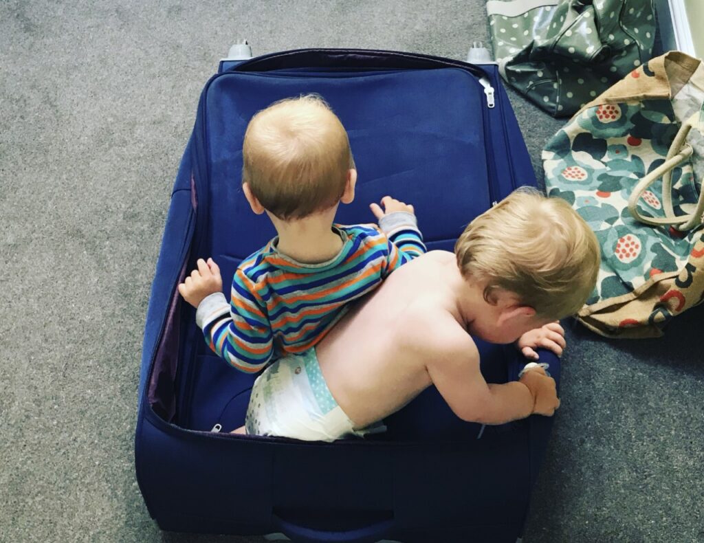 toddler twins play in a suitcase before travelling abroad 