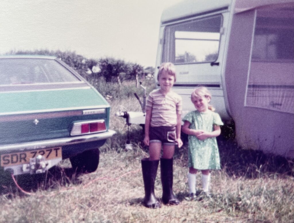 Old picture of a brother and sister aged about 6 and 3 stood outside a touring caravan