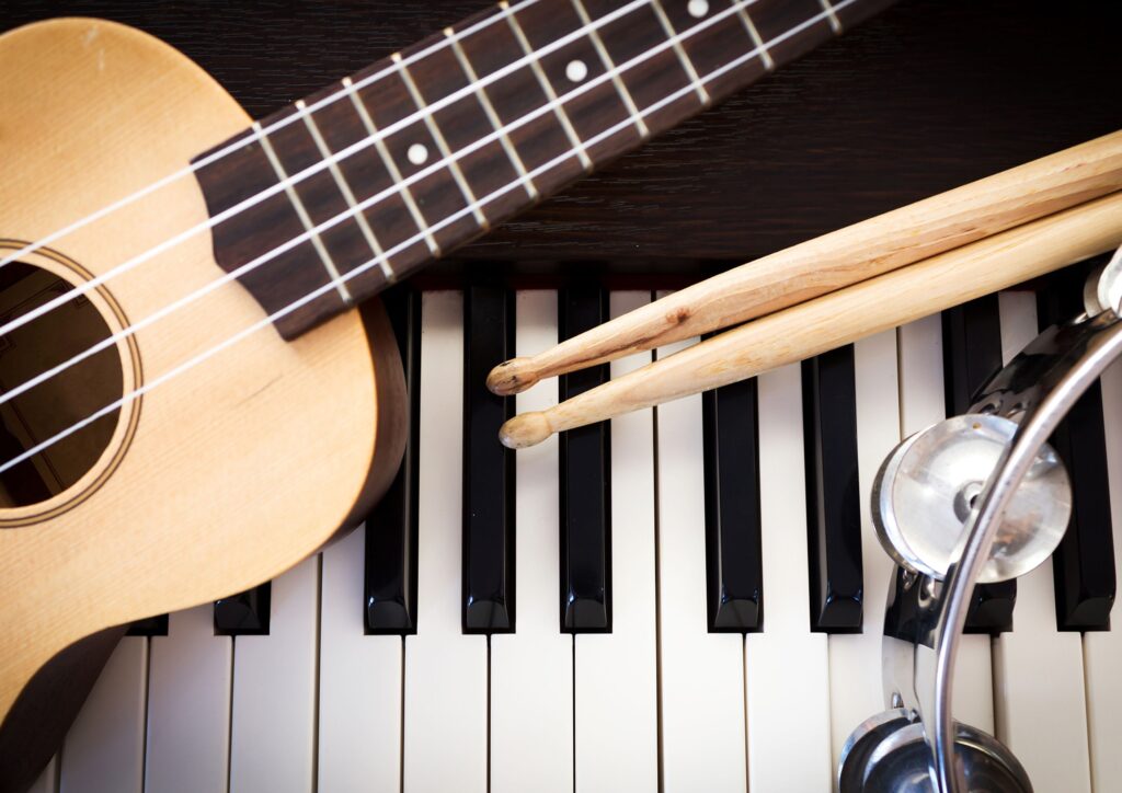 A piano with a guitar, tambourine and drumsticks resting on top of it