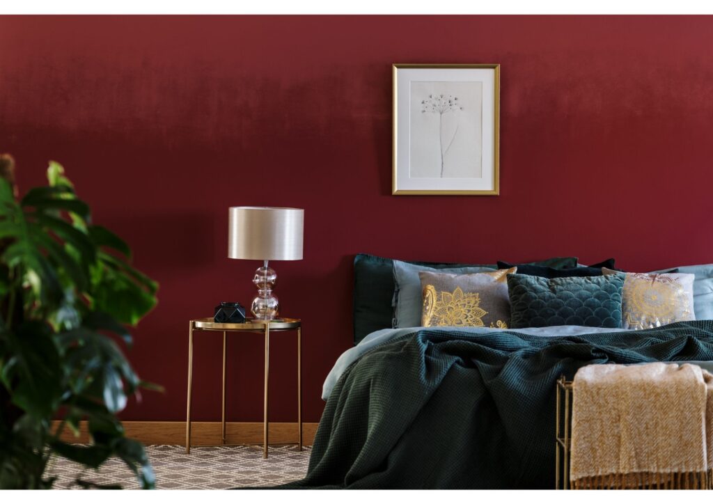 A luxurious bedroom with dark red walls and black bedding with a lamp next to the bed