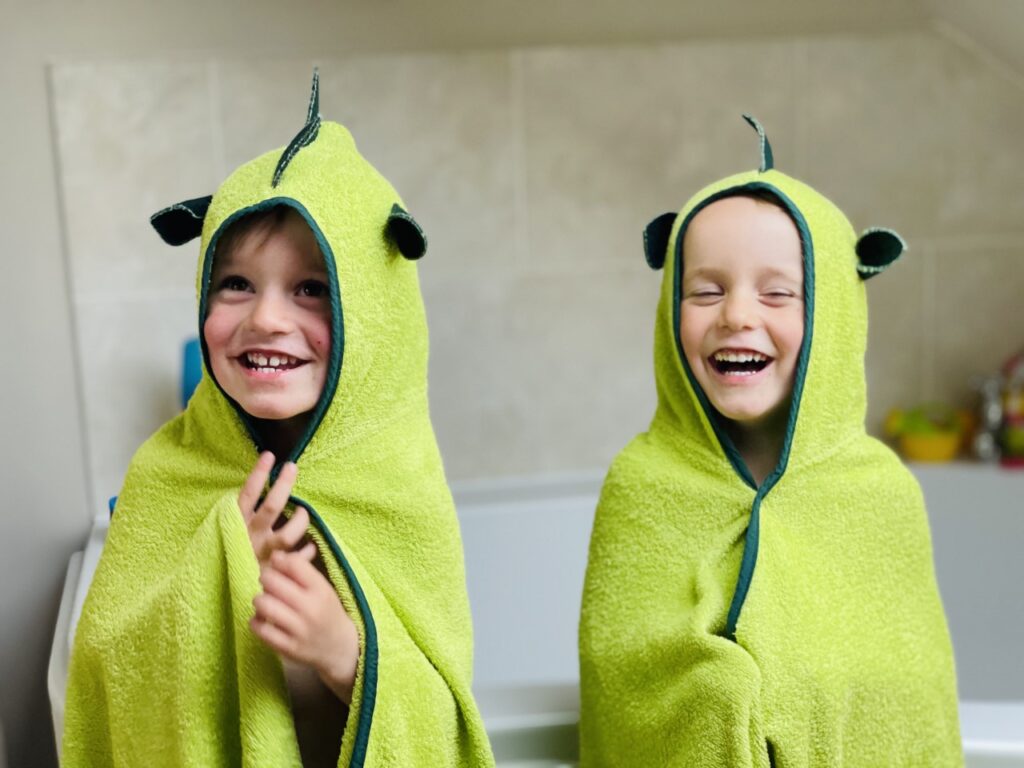 Twin three year old boys next to the bath wearing Cuddledry dinosaur hooded towels