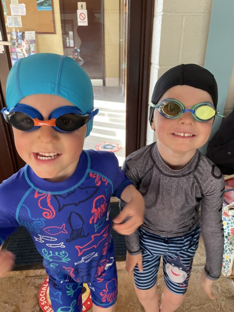 Twin brothers wear swimming costumes, hats and goggles before their lesson