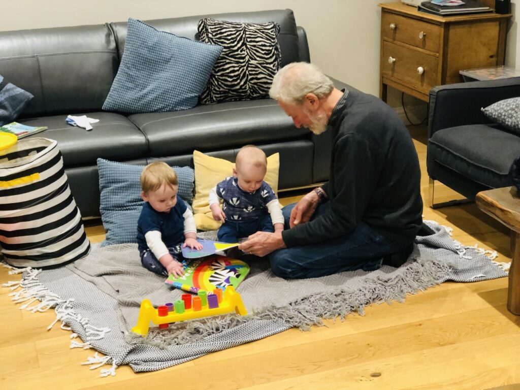 A grandad and twin nine month old twins play on the floor of a holiday home in north cornwall