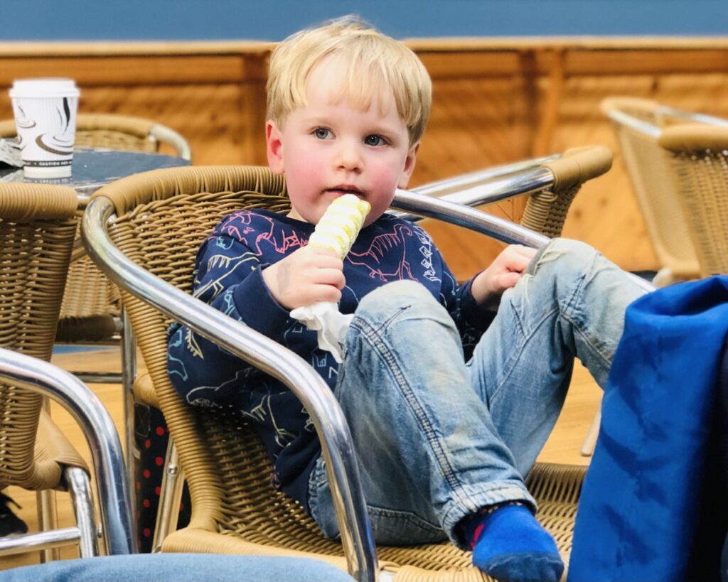 Blonde two year old boy in a chair eating a twister ice cream